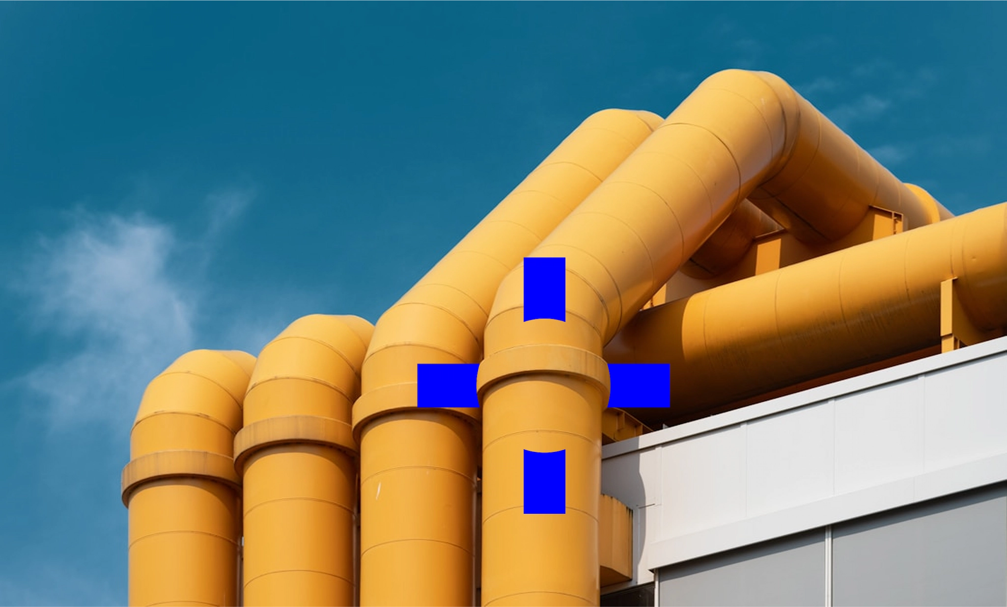 Yellow insulated industrial pipework on a petrochemical plant rooftop against blue sky